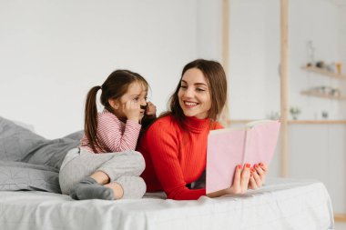 Mutlu aile annesi ve çocuğu kitap okuyor, gülümsüyor anne, bebek bakıcısı tatlı anaokulu kızına komik masallar anlatıyor, birlikte gülüyor ve yatmadan önce masallar anlatıyor.
