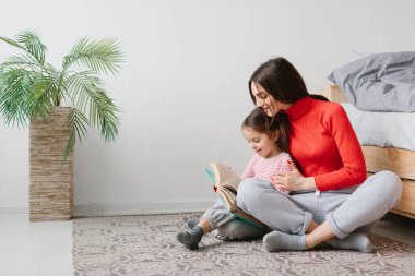 Mutlu aile annesi ve çocuğu kitap okuyor, gülümsüyor anne, bebek bakıcısı tatlı anaokulu kızına komik masallar anlatıyor, birlikte gülüyor ve yatmadan önce masallar anlatıyor.