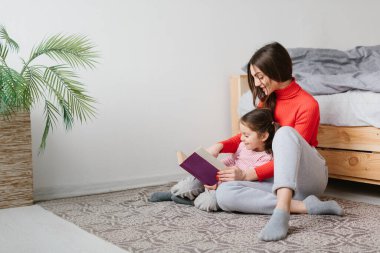 Mutlu aile annesi ve çocuğu kitap okuyor, gülümsüyor anne, bebek bakıcısı tatlı anaokulu kızına komik masallar anlatıyor, birlikte gülüyor ve yatmadan önce masallar anlatıyor.