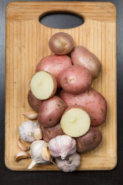Kartoffeln und Knoblauch auf Holzplatte mit schwarzem Hintergrund von oben — Stockfoto