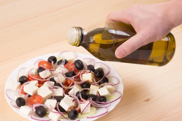Men's hand pouring olive oil into Greek salad. Wooden background