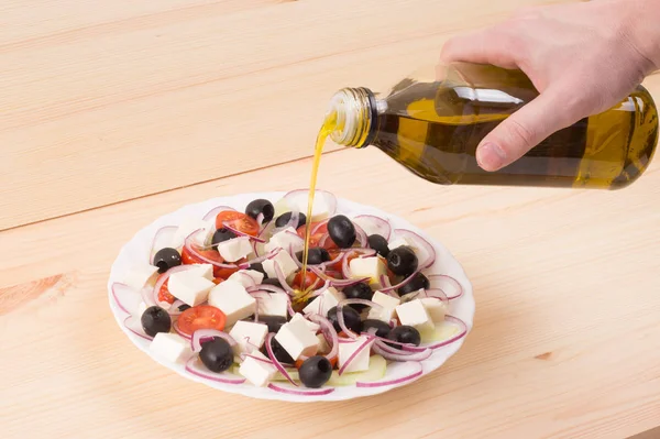 Mano degli uomini versano olio d'oliva nell'insalata greca. Sfondo in legno — Foto Stock