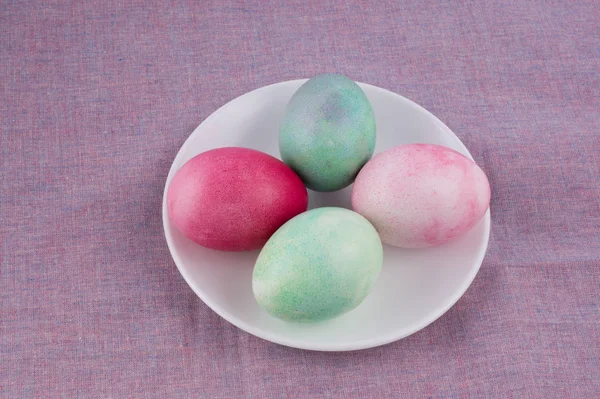 Quatre œufs de Pâques multicolores peints sur une assiette blanche et lilas — Photo