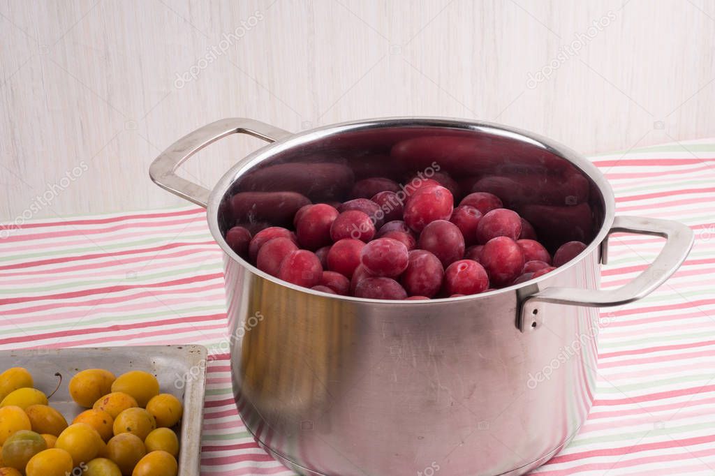 red plums in a stainless pan and  yellow ripe plums placed on al