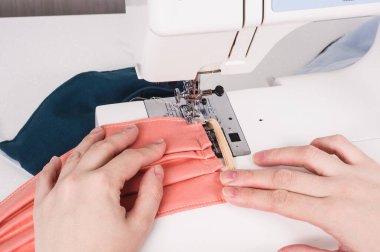 Kadın elleri dikiş makinesini kullanarak yüz maskesi durinini dikiyor.