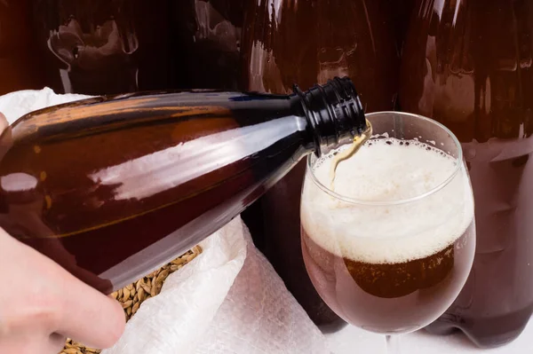 homemade beer from a plastic bottle is poured into a glass against the background of other beer bottles. Craft beer brewing from grain barley pale malt. Ale or lager from pilsner malt