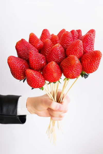 Alternative edible bouquet of berries in the hand of a man or woman, birthday, Valentine's Day, holiday, close-up. Whole strawberry fruit on wooden skewers, on a white background. Selective focus.