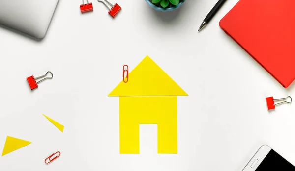 A house cut out of colored paper. There Are Scissors, A Mobile Phone, A Notepad And A Flower Nearby. The Concept Of Realizing The Dream Of Owning A Home, Buying And Building A Home.