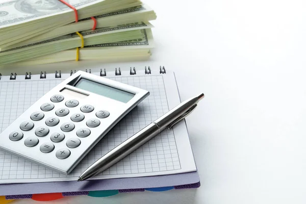 The Pen And Calculator Are On An Open Notebook Or Notepad. Next To It Is A Stack Of American Dollar Bills. The Concept Of Financial Accounting, Bribery And Corruption.