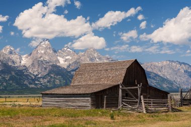 Engebeli dağ zirveleri altında yıpranmış ahşap ahır