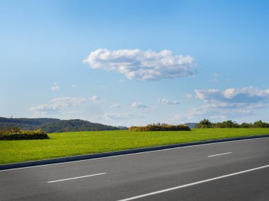 Asfalt yolu olan sonbahar manzarası, gökyüzünün altında bulutlu yeşil çimen