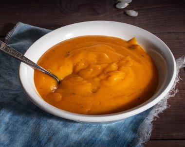 Koyu beyaz bir tabakta, ahşap tepside servis edilen kabak çorbası.