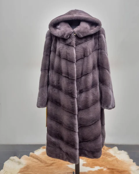 Purple mink fur coat with a hood, cut with transverse stripes, on the construction site of the exhibition hall