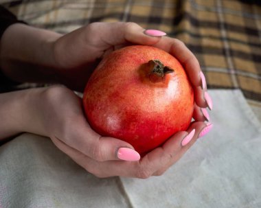 Kızın elleri, ekose kumaşın arka planında olgun bir nar tutuyor.