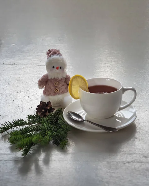 Té con limón en una taza blanca. La mesa rústica está decorada con ramas de abeto y una figura de muñeco de nieve . — Foto de Stock