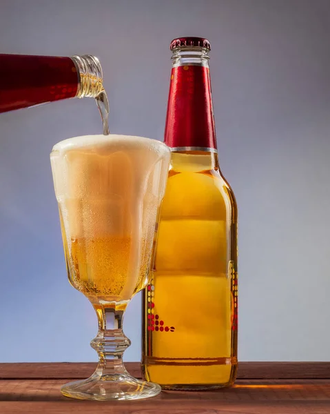 Bouteille en verre et verre avec bière en mousse coulée sur un fond bleuté — Photo
