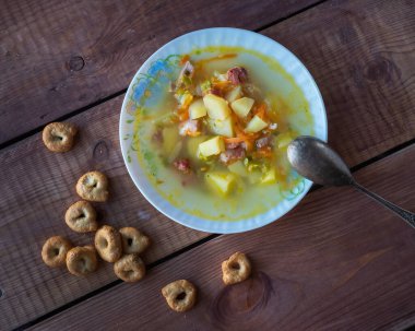 Yuvarlak tabakta sıcak çorba, bezelye, füme et ve tahtadan bir masada mısır gevreği.