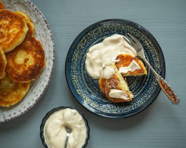 Ev yapımı taze pişmiş peynirli kekler tabakta ekşi krema, tabakta tatlı çatalı