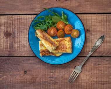 Omletle ev yapımı kahvaltı ve mavi tabakta taze sebzeler, ahşap tepside servis.