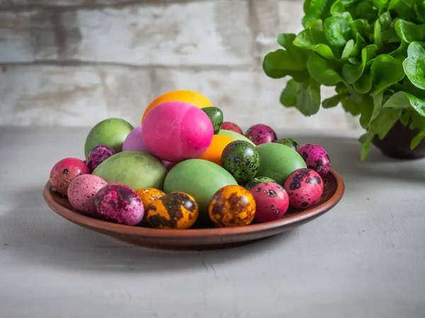 A pile of boiled eggs painted in different colors on a ceramic brown plate. Fresh salad in the background. Easter