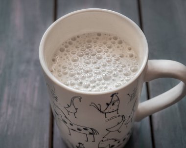 Beyaz bardakta kapuçino. Kahvenin yüzeyinde süt köpükleri var.