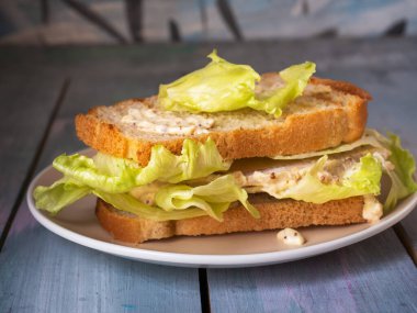 Jambonlu, peynirli ve soslu büyük bir sandviç ahşap masasında yuvarlak bir tabakta yer alır.