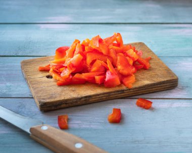 Mutfak tahtasında doğranmış kırmızı dolma biber ve ahşap saplı bir bıçak mavi ahşap bir masada yatıyor.