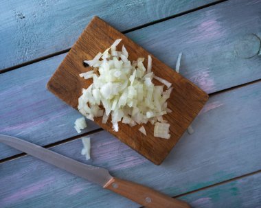 Doğranmış soğan küpleri mavi bir masa üzerinde küçük bir tabakta ve bir mutfak bıçağı, üst manzara