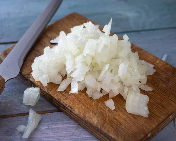 Preparation for cooking, chopped onions on a cutting board on a blue wooden table, shot from a close distance