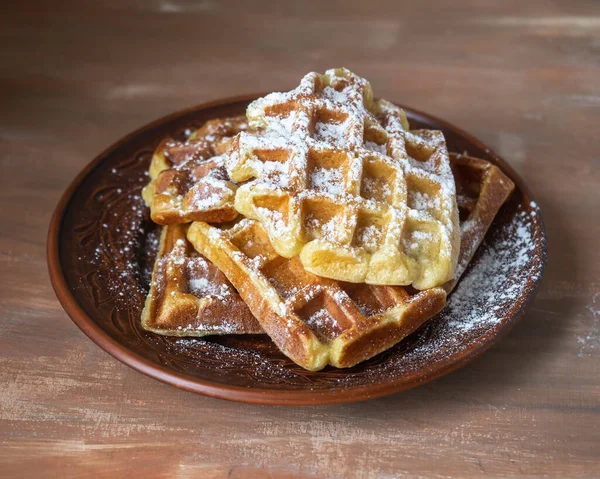 Tatlı tatlı. Kahverengi bir masadaki seramik tabakta kaygan şekerli ev yapımı waffle 'lar.