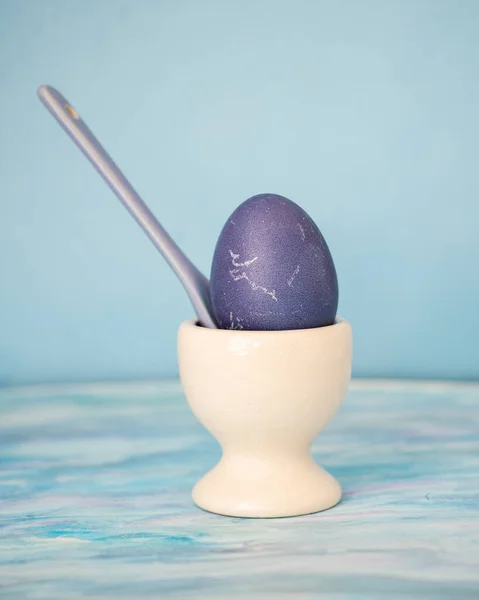 Egg on a white ceramic stand for lilac eggs and a lilac ceramic spoon in a stand with an egg on a blue background