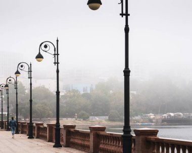 Şehirde yoğun bir sis, denize ve şehre tepeden bakan sabah manzarası, terk edilmiş bir kız figürü.
