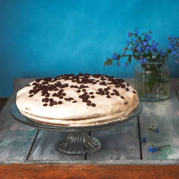 Hausgemachte Torte mit Sahne auf einem Ständer, im Hintergrund ein Glas mit blauen Veilchen — Stockfoto