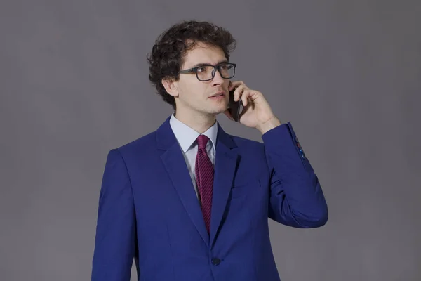 Young man in blue suit and glasses standing and talking by mobile phone