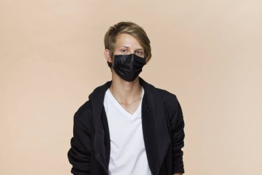 Kahve arka planında maskeli bir gencin portresi virüse karşı korur, siyah maske.