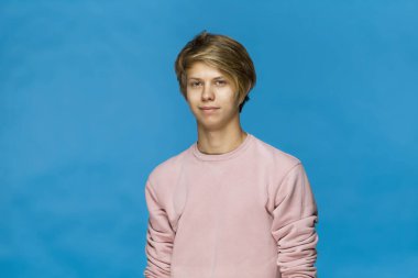 Yakışıklı, mutlu, pembe bluz giyen genç adam mavi duvara karşı stüdyo resmi giyiyor.