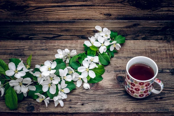 Une branche de fleurs de pomme et une tasse de thé sur fond de bois — Photo