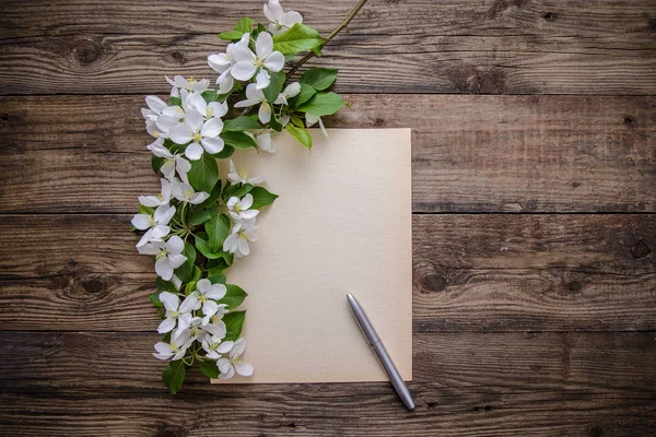 Une branche de fleurs de pomme, stylo et feuille de papier sur fond en bois — Photo