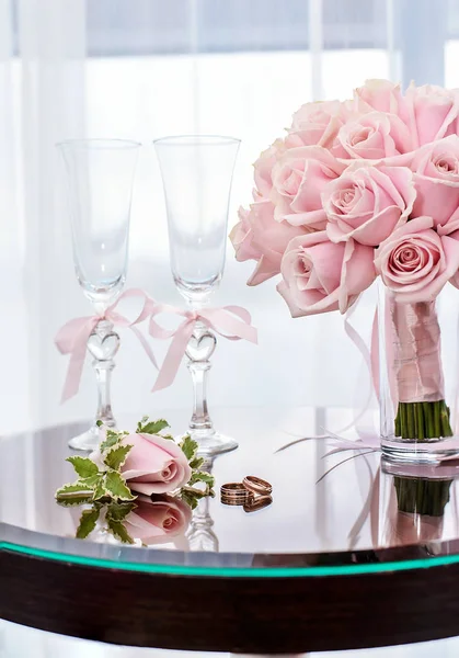 Wedding glasses next to the boutonniere, rings and bouquet