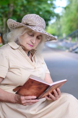 Yaşlı bir kadın parkta bir kitap okur