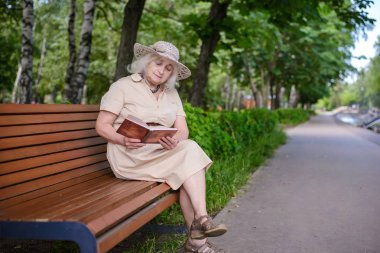 Yaşlı bir kadın parkta bir kitap okur