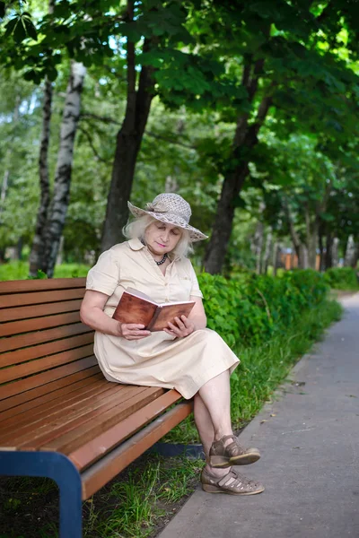 An elderly woman reads a book in the park Stock Picture