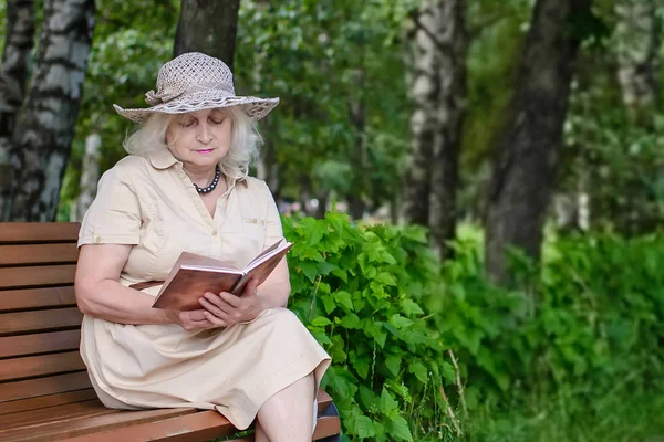 Una anciana lee un libro en el parque —  Fotos de Stock