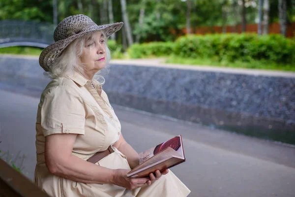 Uma mulher idosa lê um livro no parque — Fotografia de Stock