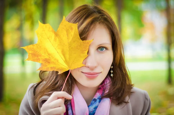 Девушка смотрит сквозь желтый осенний лист — стоковое фото