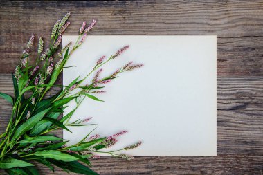 Bir kağıt yaprağına ve ahşap arka plan üzerinde küçük pembe çiçekler