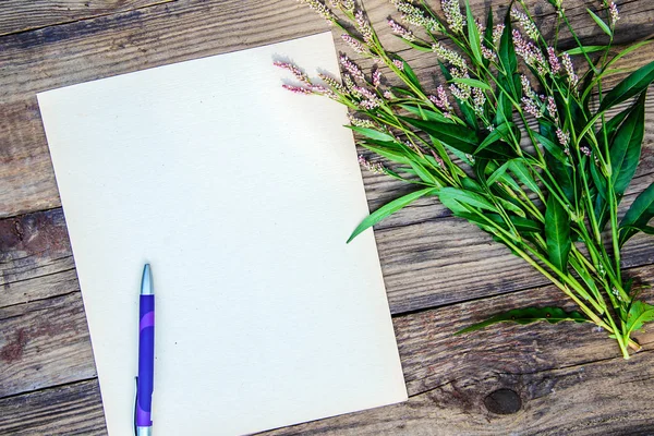 Карточка: лист бумаги, ручка и маленькие цветы на деревянной спинке — стоковое фото