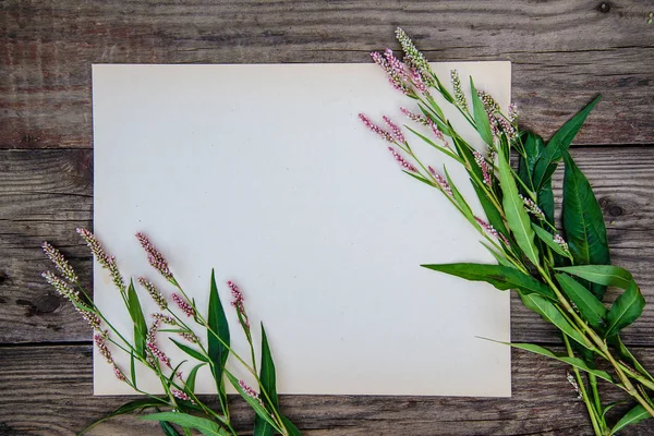 List papíru a malé růžové květy na dřevěné pozadí — Stock fotografie