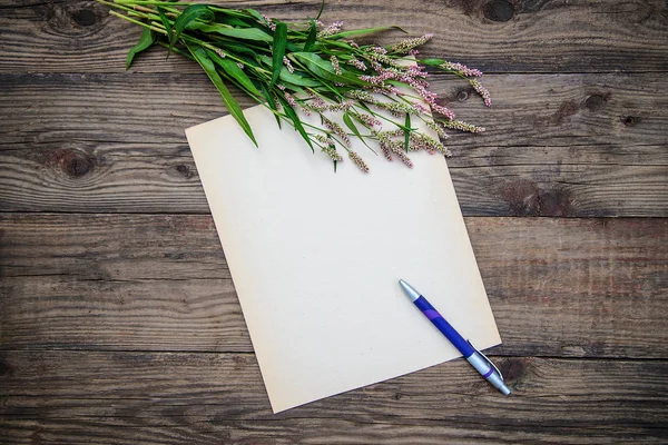 Carte : feuille de papier, stylo et petites fleurs sur fond bois — Photo