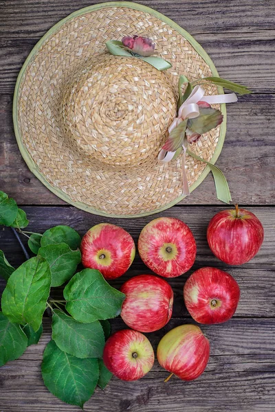 Red apples and straw hat on wooden background